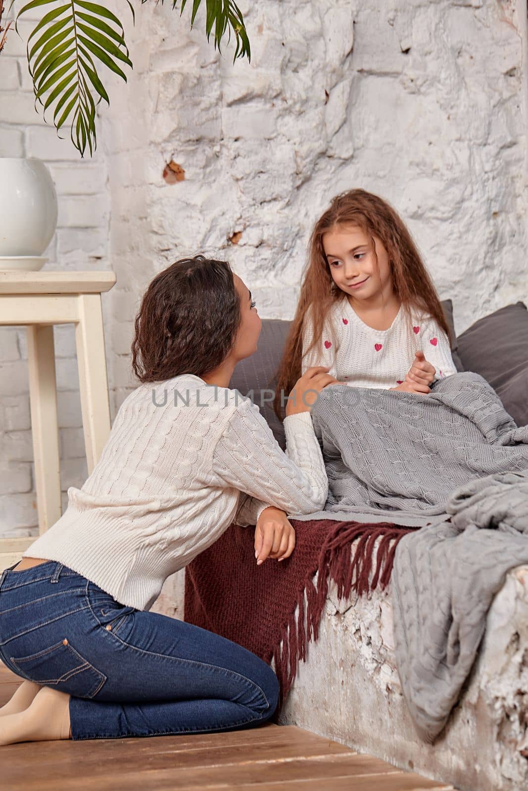 Mother and daughter sitting on sill near window in room. They show emotions and have fun