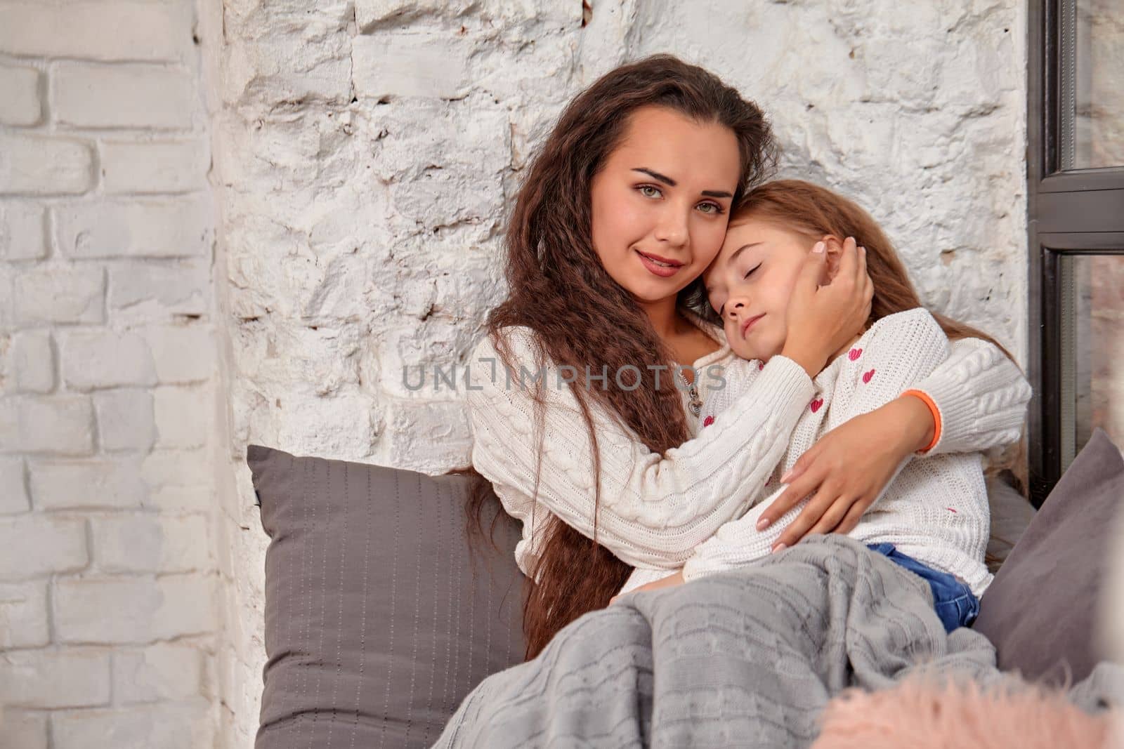 Mother and daughter sitting on sill near window in room. The daughter sleeping on mother's hands