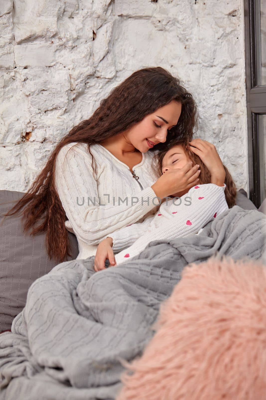 Mother and daughter sitting on sill near window in room. The daughter sleeping on mother's hands