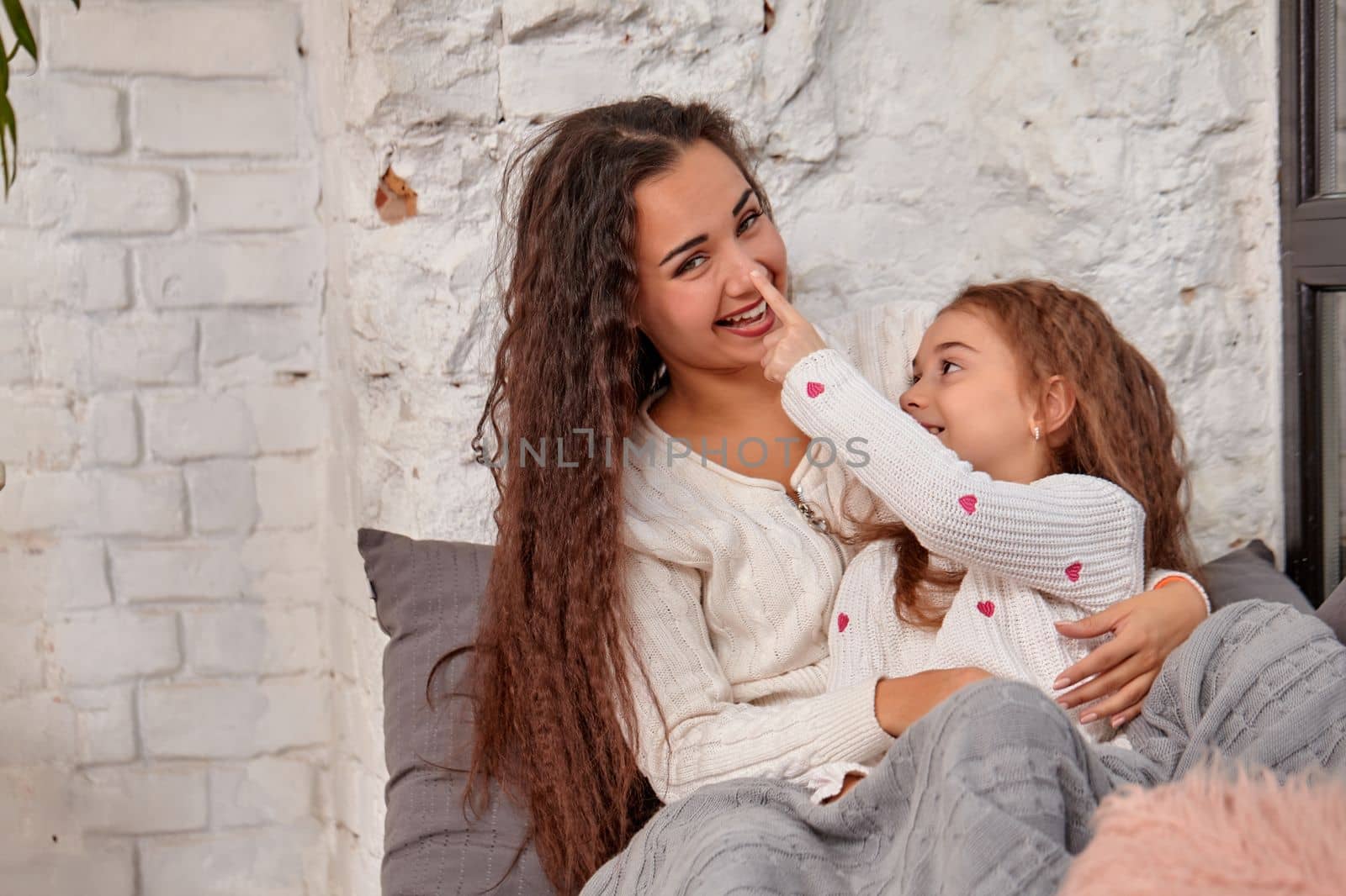 Mother and daughter sitting on sill near window in room. They show emotions and have fun