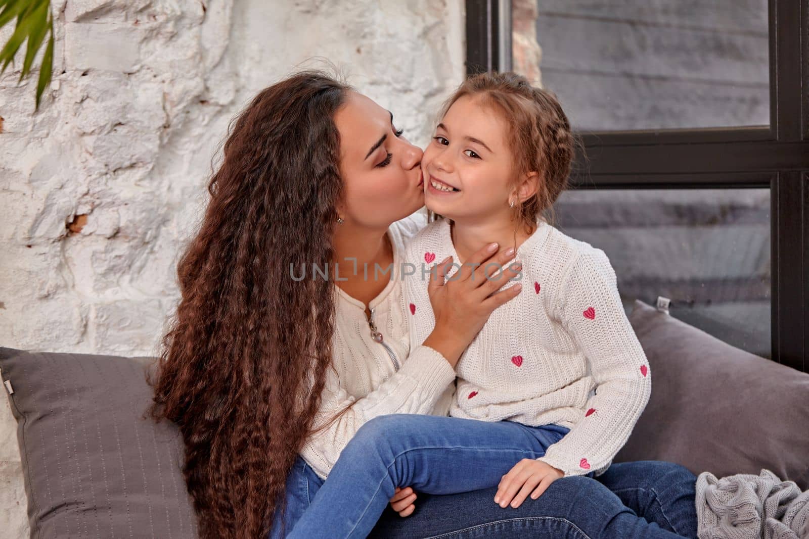 Mother and daughter sitting on sill near window in room. They show emotions and have fun