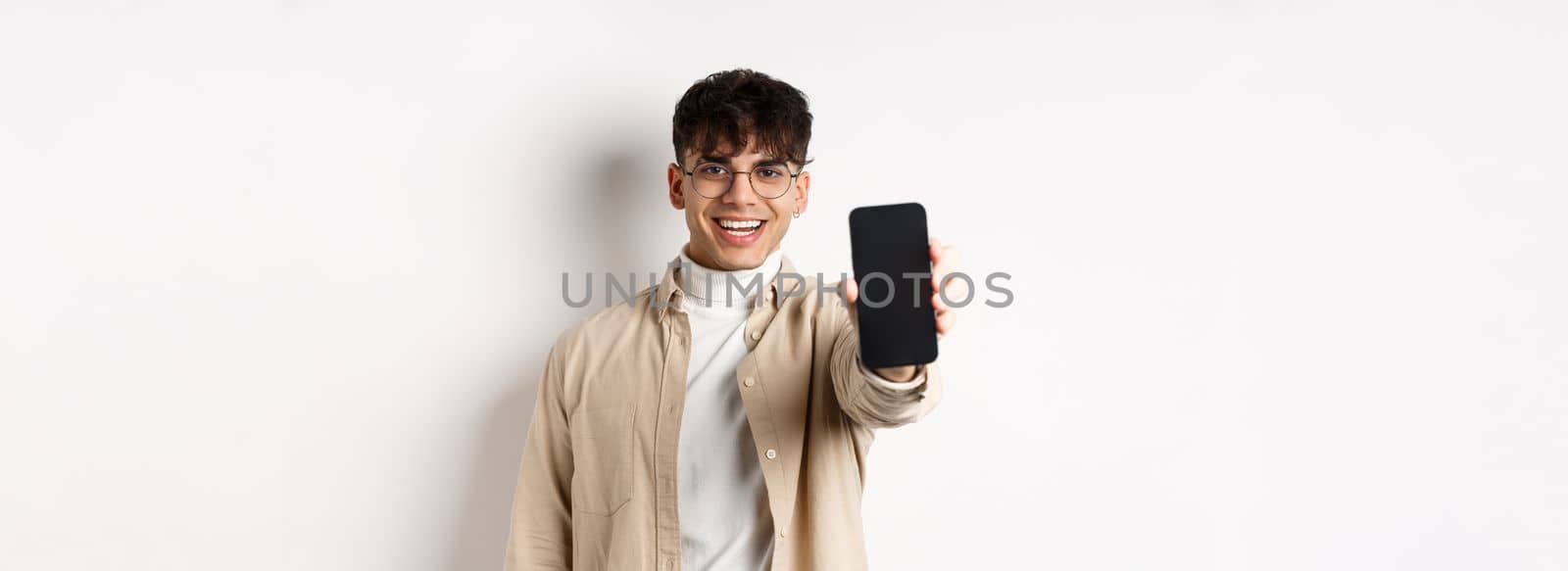 Handsome young man showing empty smartphone screen, standing on white background. Copy space