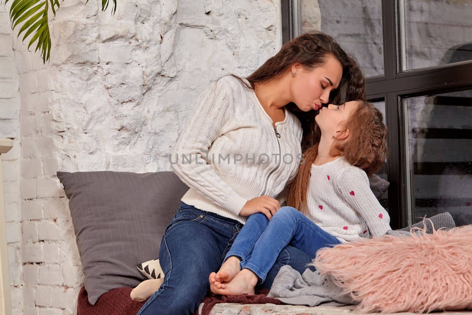 Mother and daughter sitting on sill near window in room by nazarovsergey