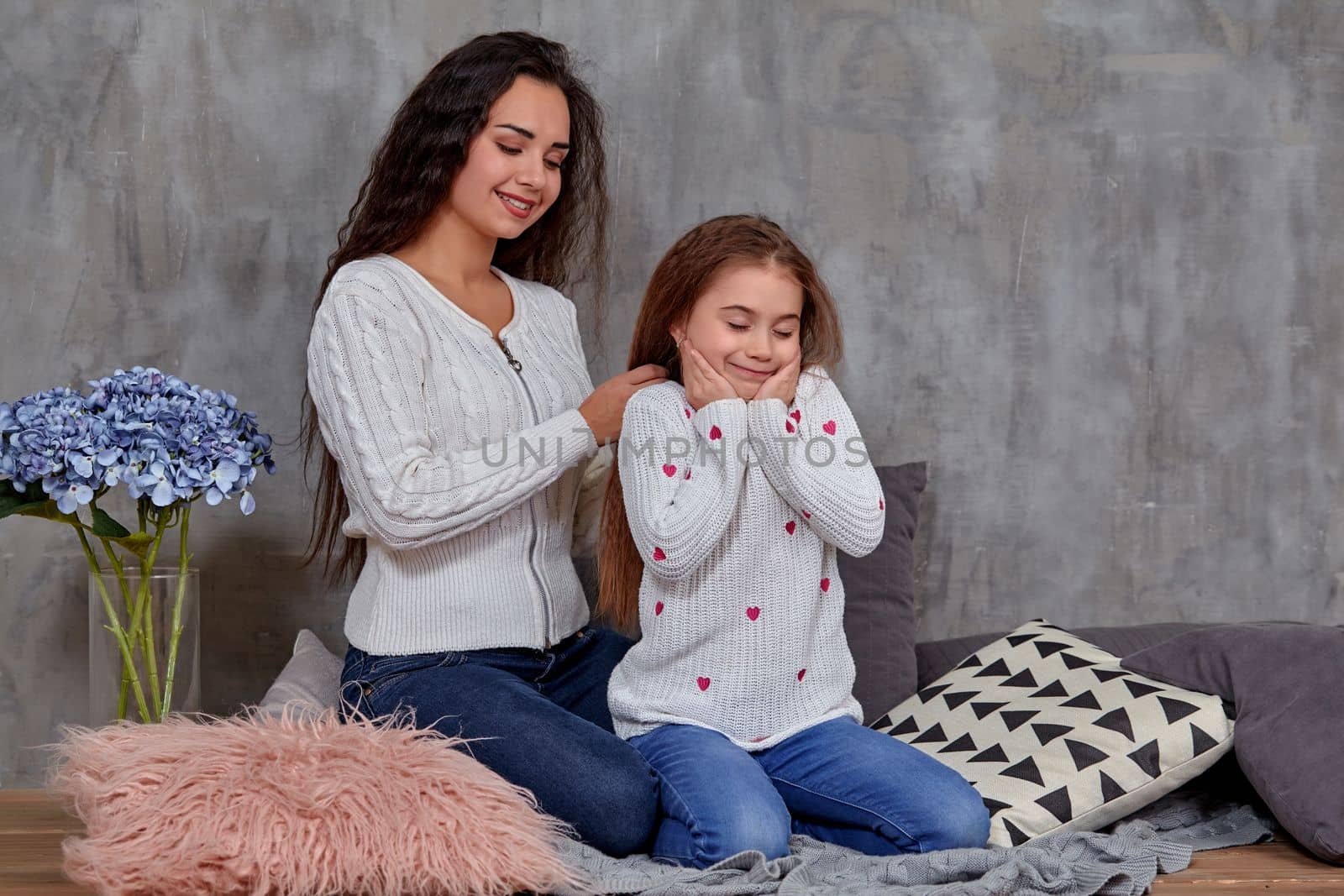 Eemotions of a beautiful young mother and her little daughter who spend time together. They sit on the floor and mom cares for her daughter's hair