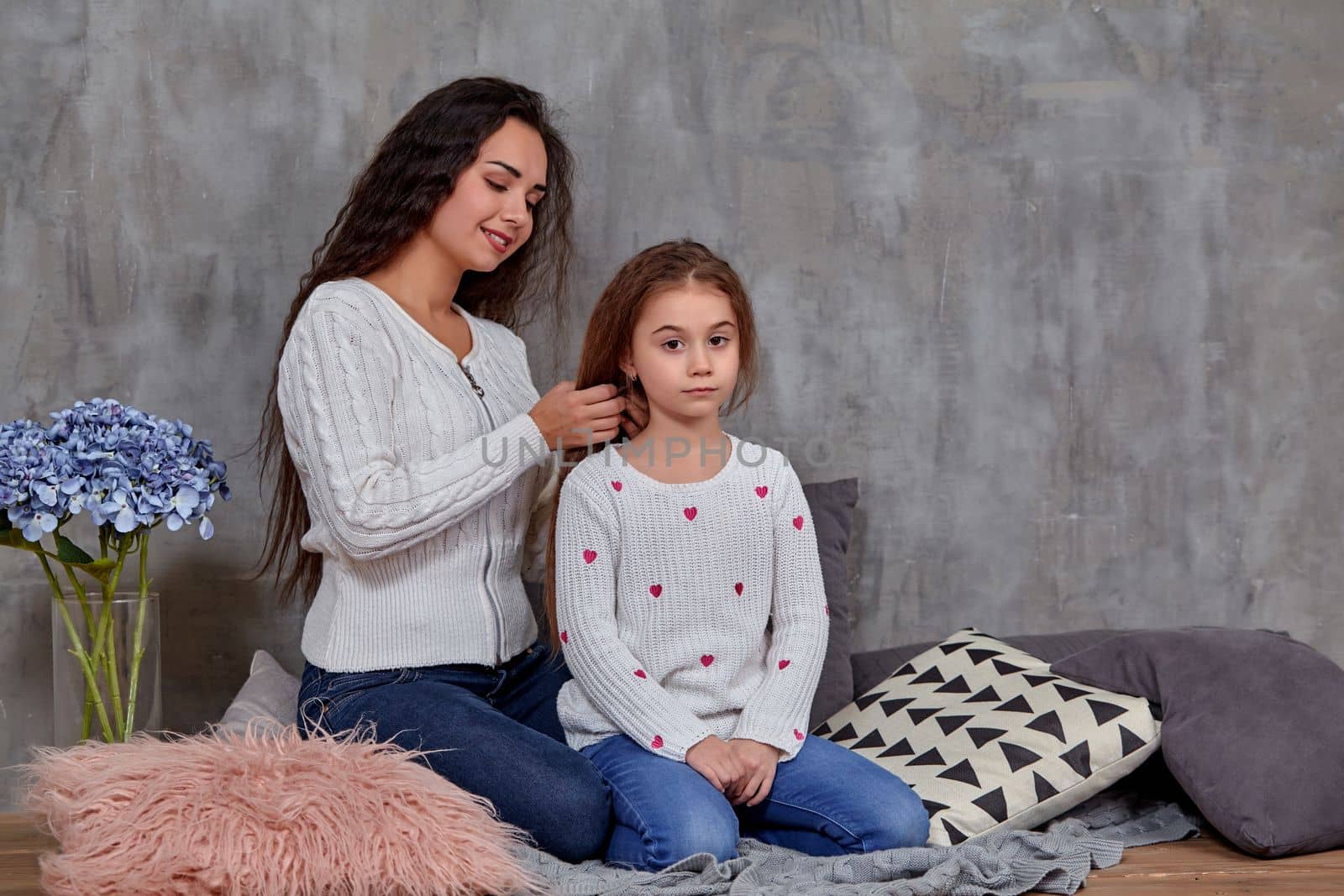 Eemotions of a beautiful young mother and her little daughter who spend time together. They sit on the floor and mom cares for her daughter's hair