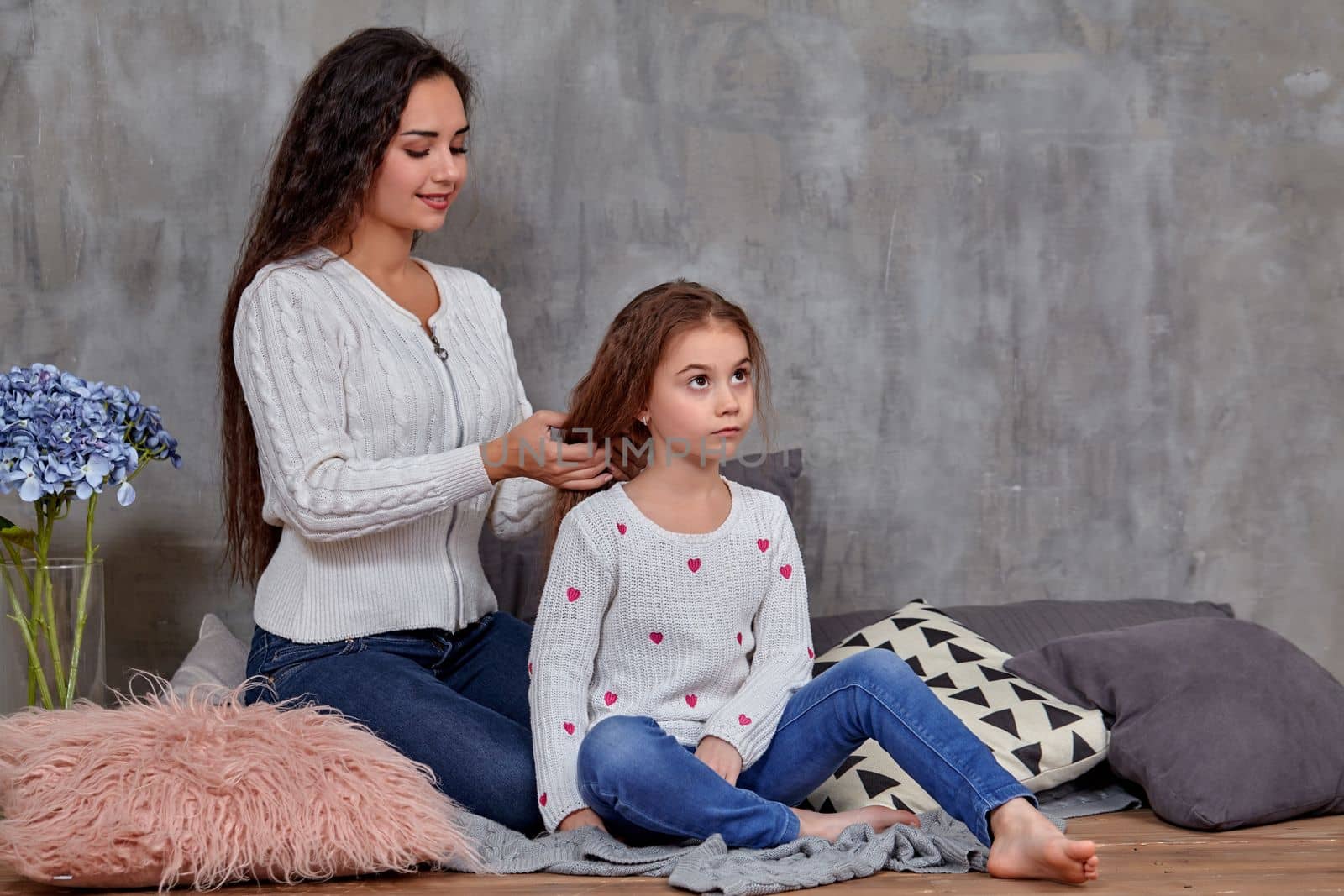 Eemotions of a beautiful young mother and her little daughter who spend time together. They sit on the floor and mom cares for her daughter's hair