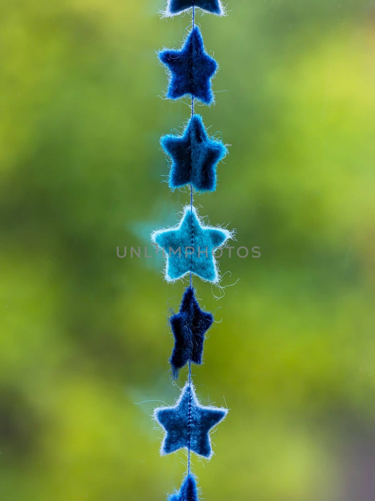 Garland with stars made of felt on a chain with thread released in front of natural green tones of a hedge