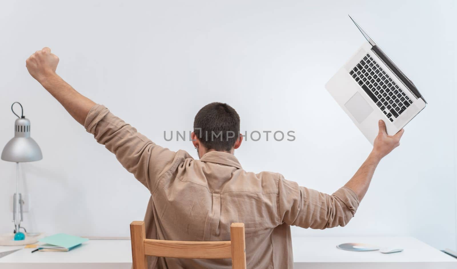 Unrecognizable young man with laptop celebrating with raised arms success at work in home office. High quality photo
