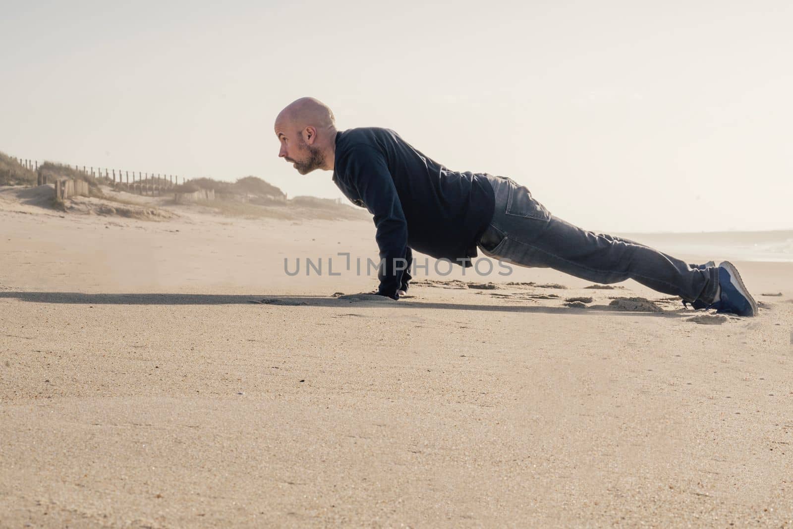 Young guy doing push ups alone on the beach. Morning photo, wearing casual jeans with copy space by papatonic