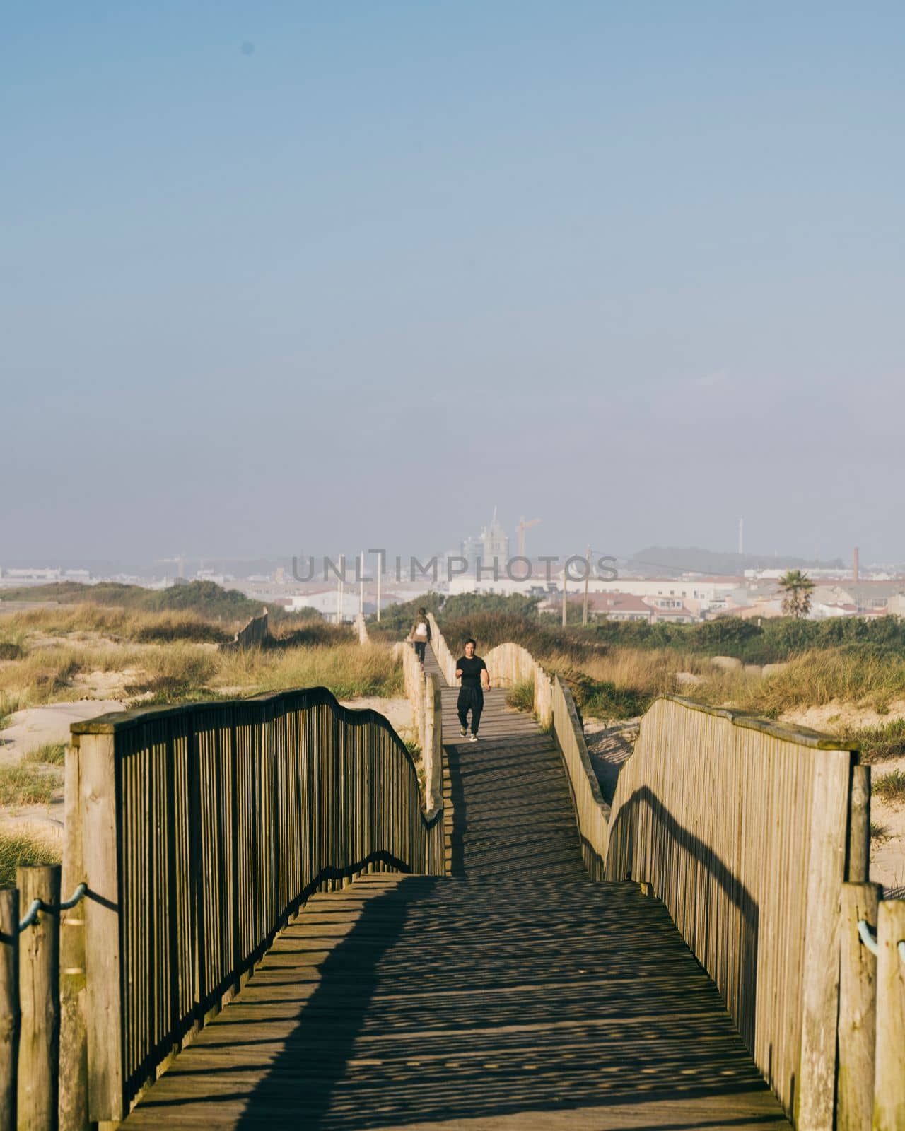 People on a walk along a wooden pier at the dune beach into the sunset. Praia de Silvalde , Portugal.