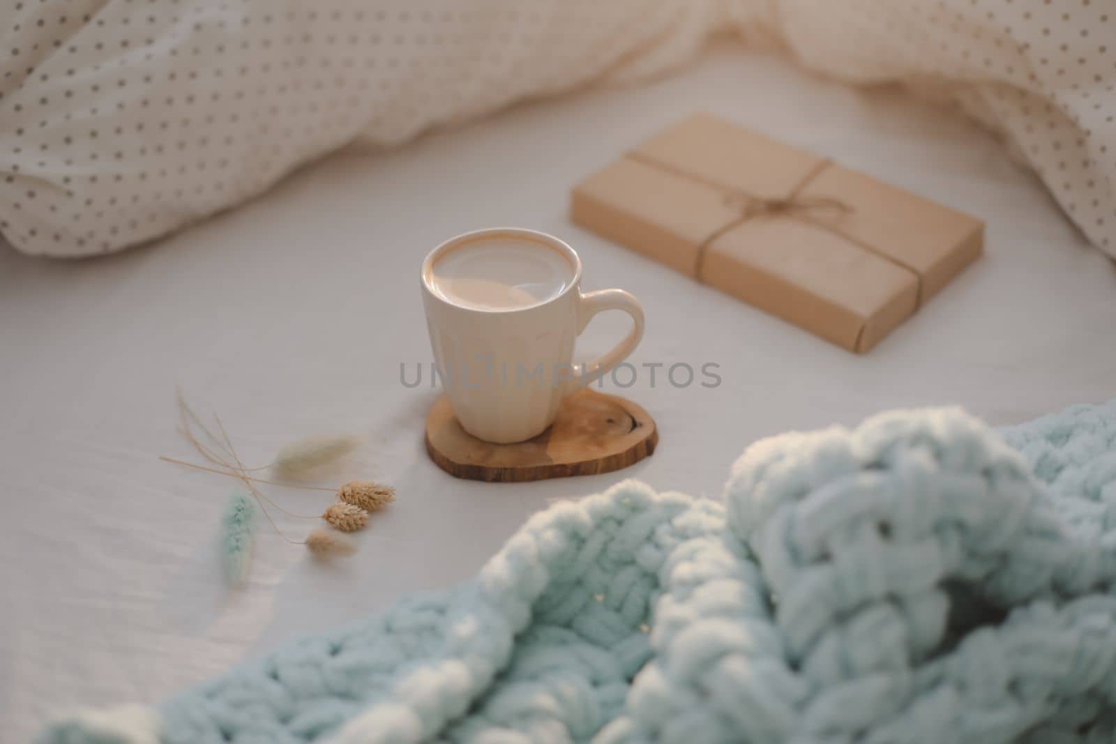 Cup of coffee with milk and gift box in bed with plaid, copy space. Flat lay, top view. morning in bed concept composition. 