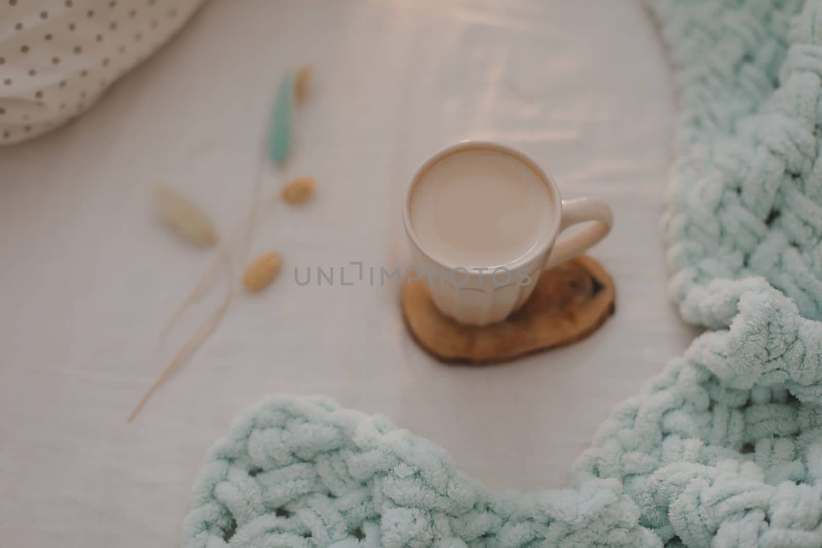 Cup of coffee with milk on the bed with white linens and blanket. Morning coffee in bed concept