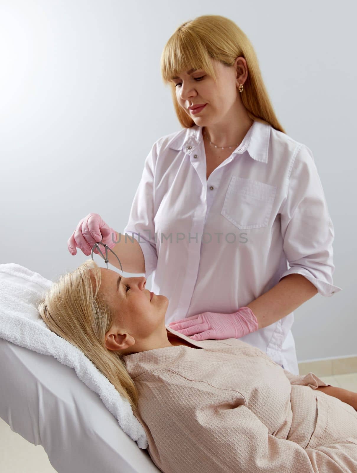 Woman getting her eyebrows angled by a beautician in beauty salon with instrument