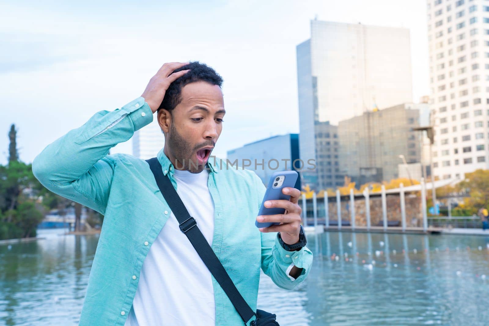 Young black man in the street looking at the phone with a surprised expression. High quality photo