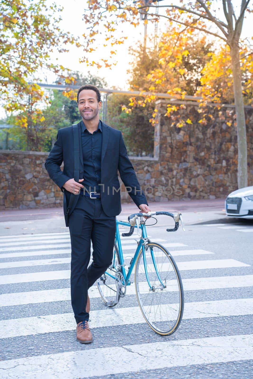 Stylish African American businessman in suit crossing the street with the bicycle. Business and transport concept. High quality vertical photo