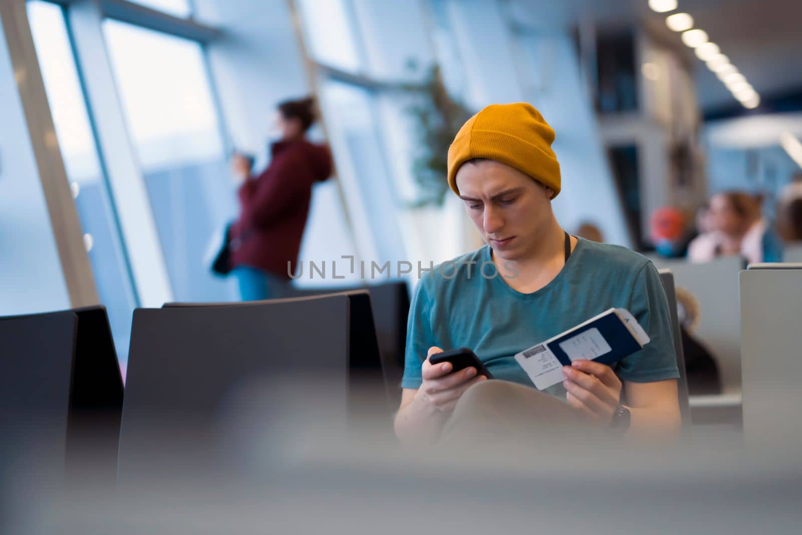 A young man sits at the airport and checks in for the next flight via an app on his phone, waits for the plane and works while traveling.
