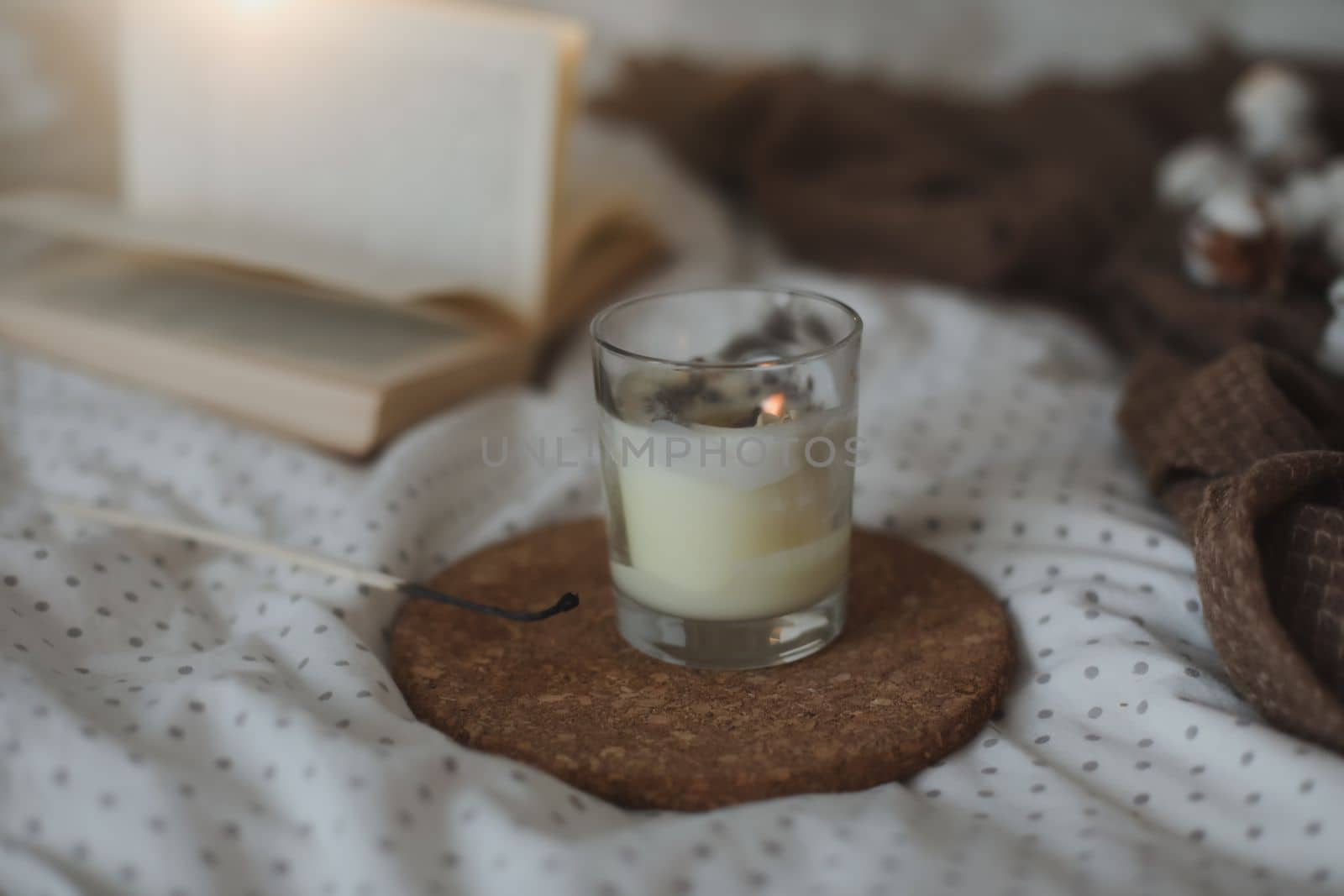 Cozy still life interior details with a book, candle and a cotton flower in warm soft bed. Sweet home