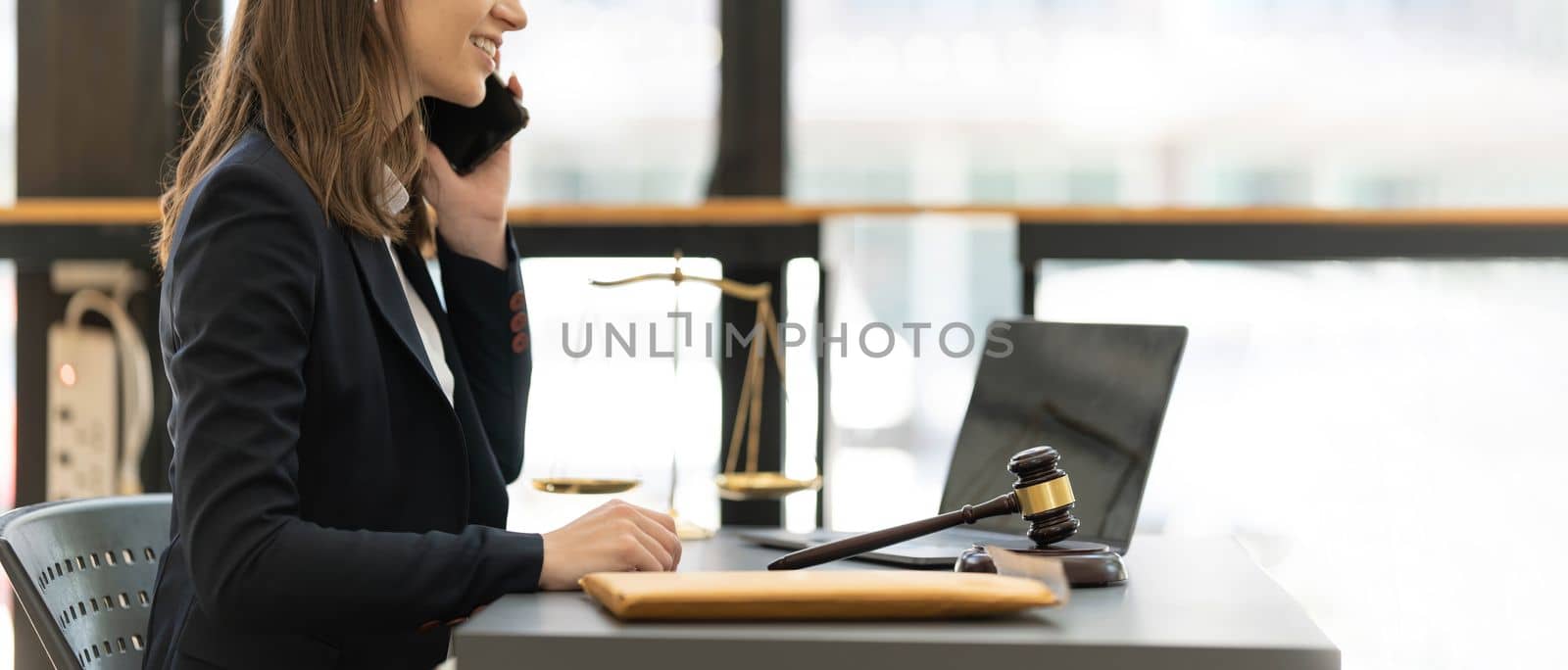 Lawyer woman talking mobile phone and working on tablet and laptop on table in office...