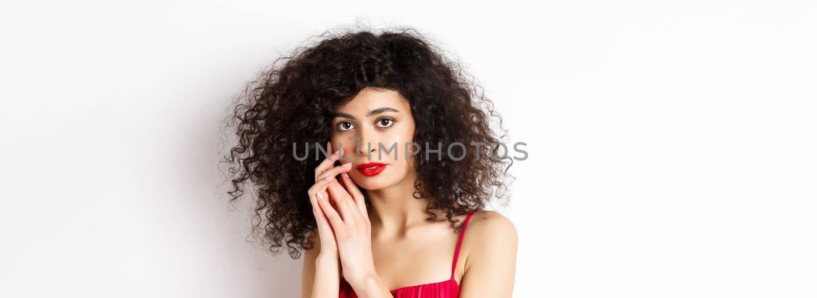 Close-up of tender romantic woman, gently touching face and looking sensual at camera, white background.