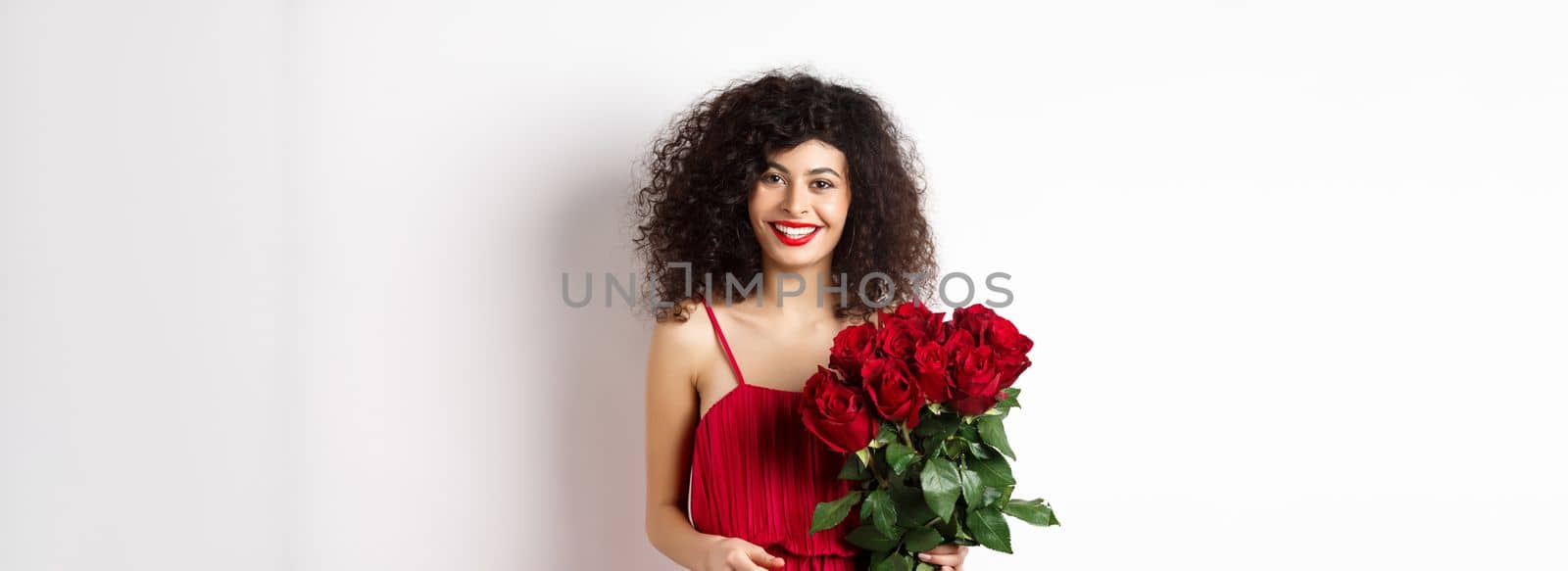 Elegant smiling lady with red lips and dress, holding bouquet of roses and looking happy, white background by Benzoix