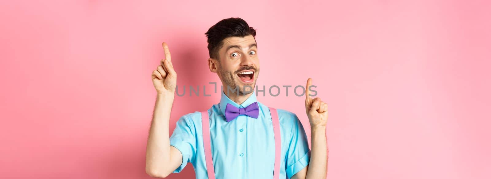 Cheerful guy with french moustache pitching an idea, dancing and raising fingers up, having solution, standing happy over pink background.