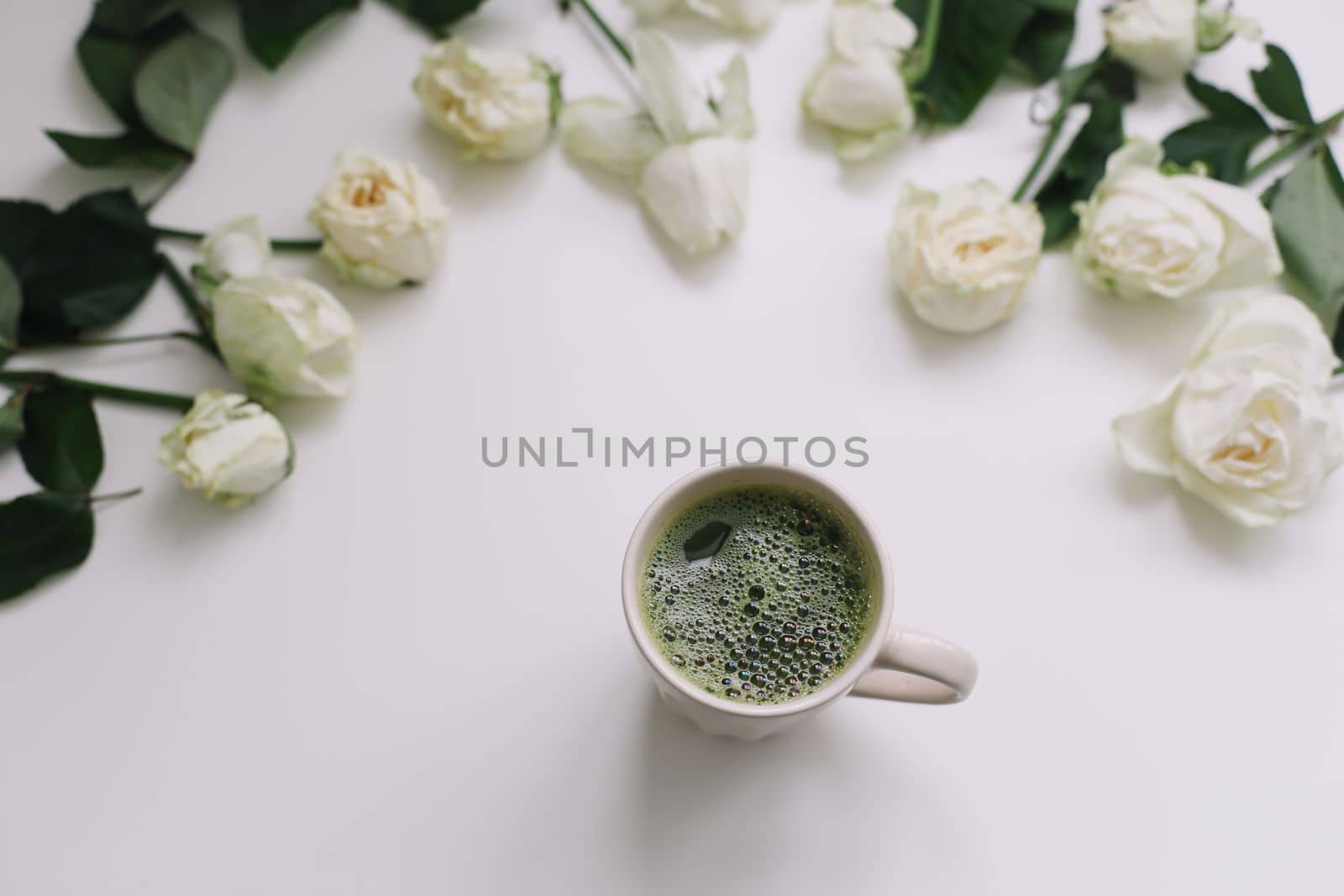 A cup of green tea with white roses on white background. Flatlay, top view, copy space. 