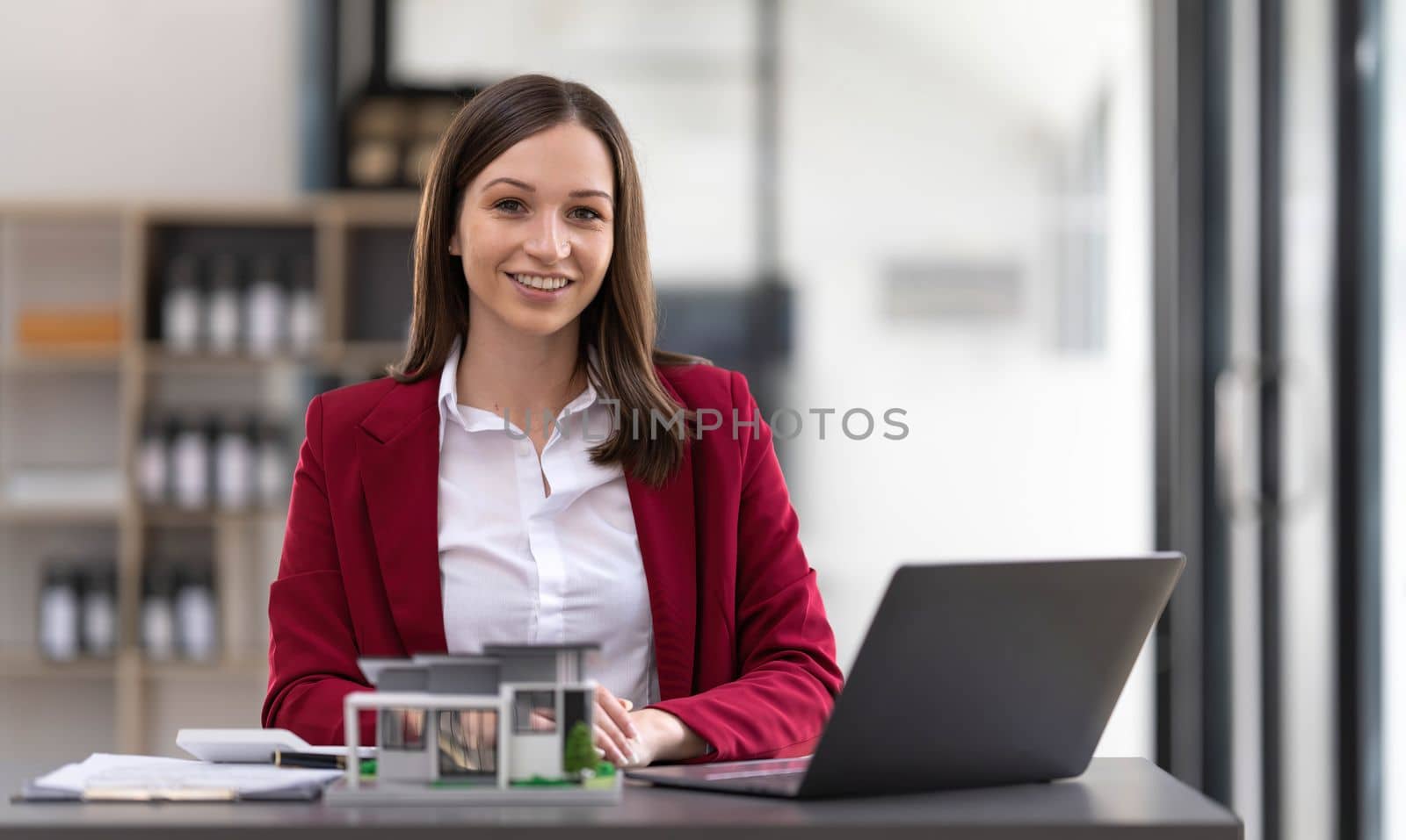 Young Asian real estate agent worker working with laptop at table in office and small house beside it...