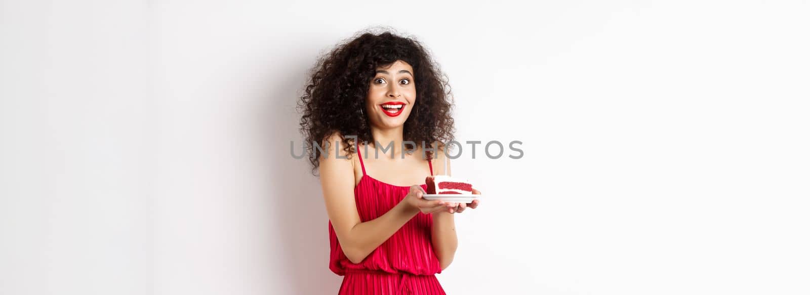 Birthday girl holding cake and making wish, smiling and celebrating, wearing festive red dress, white background by Benzoix