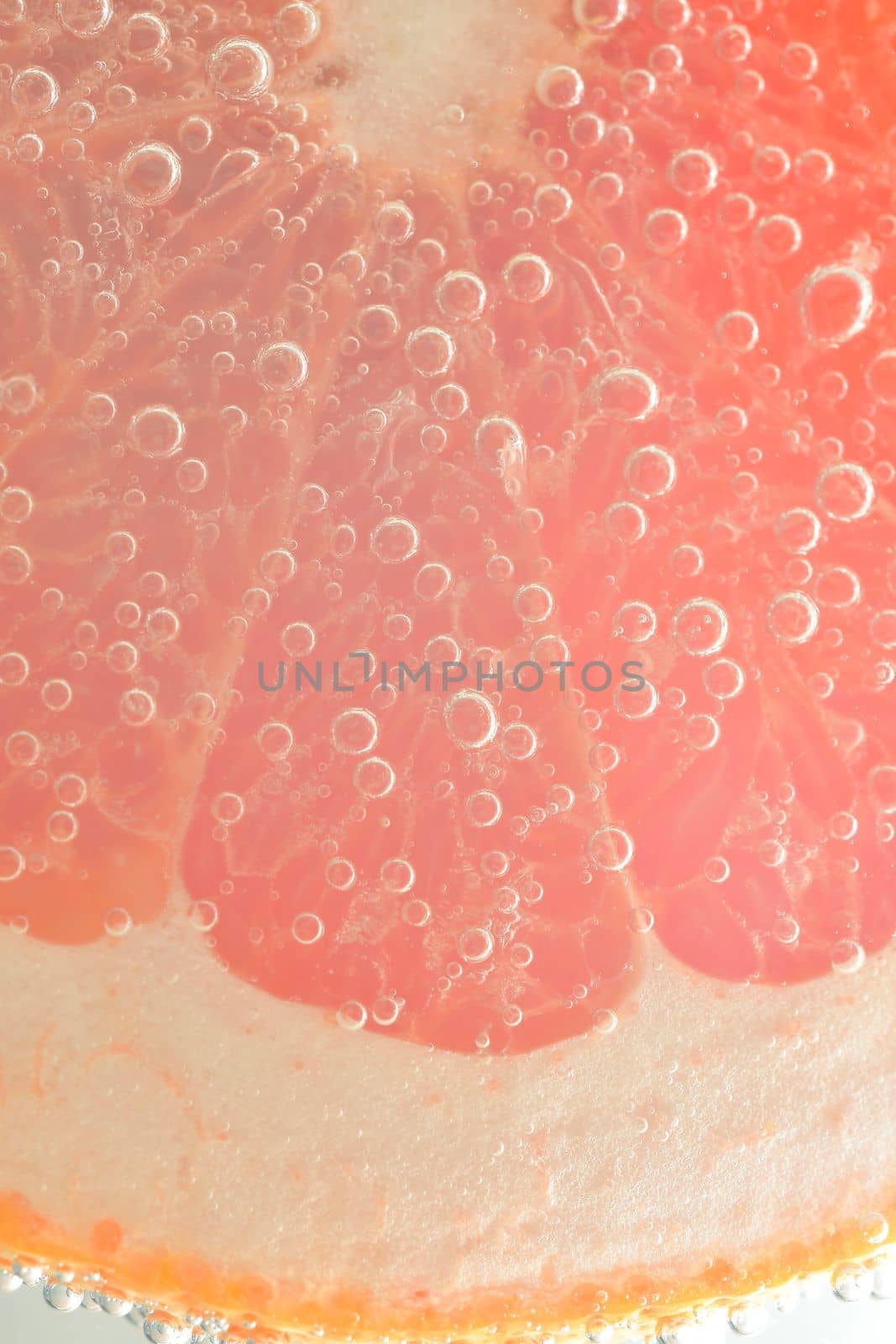 Close-up of juicy grapefruit slice on white background. Slice of red grapefruit in sparkling water on white background, close-up. Vertical macro image.