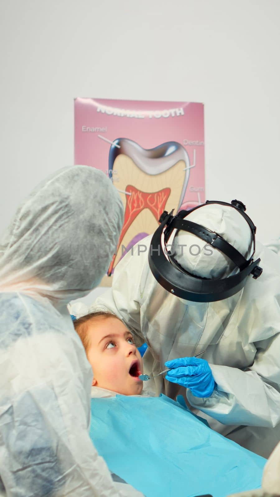 Dentist in ppe suit standing near girl patient talking with mother by DCStudio