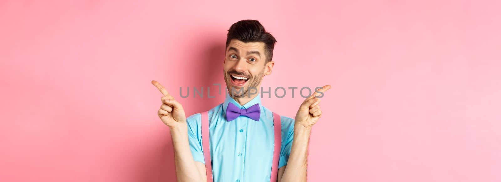 Handsome funny guy pointing fingers aside, showing left and right logo and smiling, recommending two choices, standing on pink background.