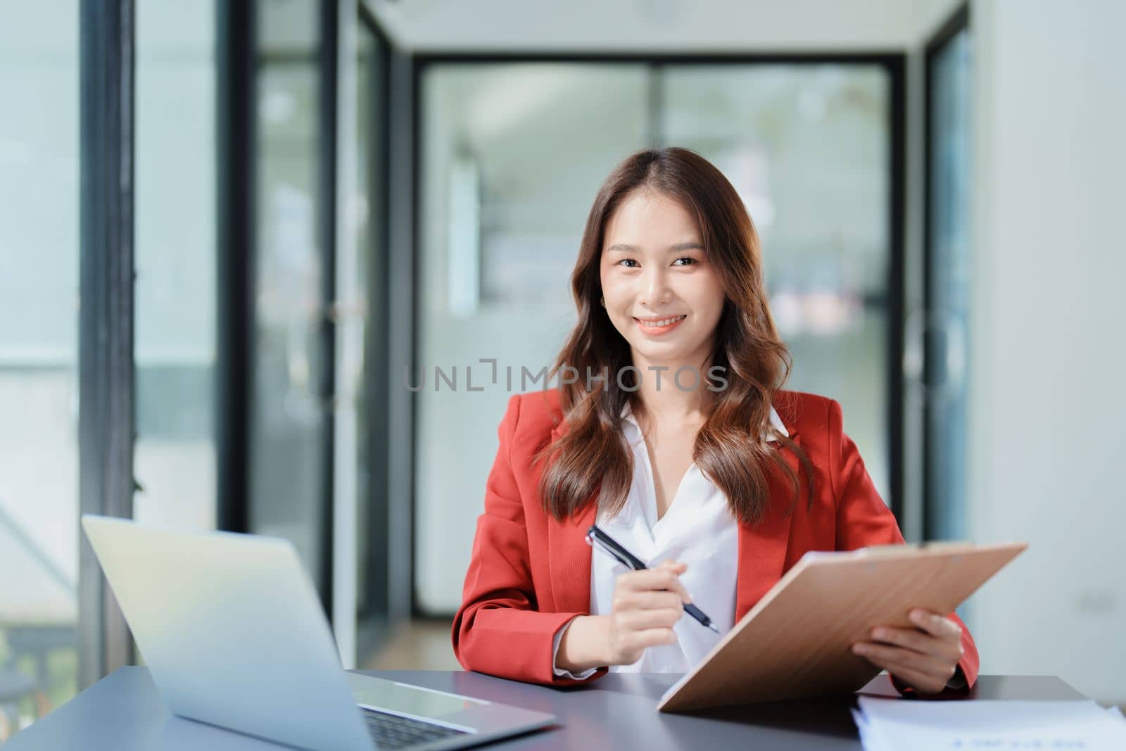 Portrait of a thoughtful Asian businesswoman looking at financial statements and making marketing plans using a computer on her desk.