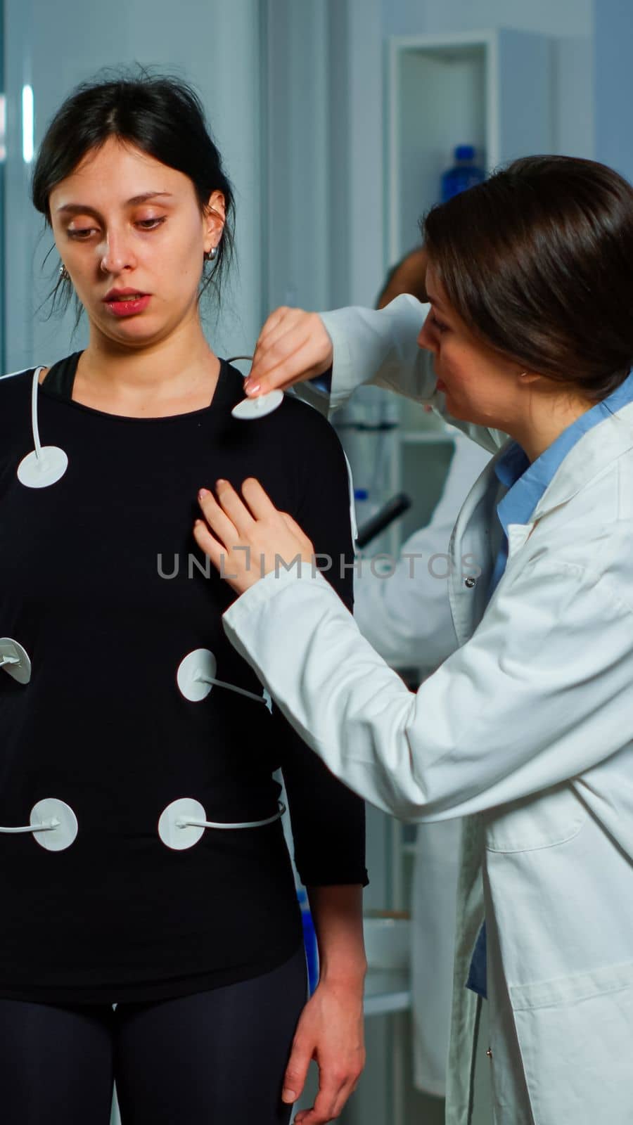 Scientist researcher preparing woman patient for endurance test attaching electrodes on professional body equipment. Team of doctors monitoring health of patinet, vo2, ekg scan runs on computer screen.