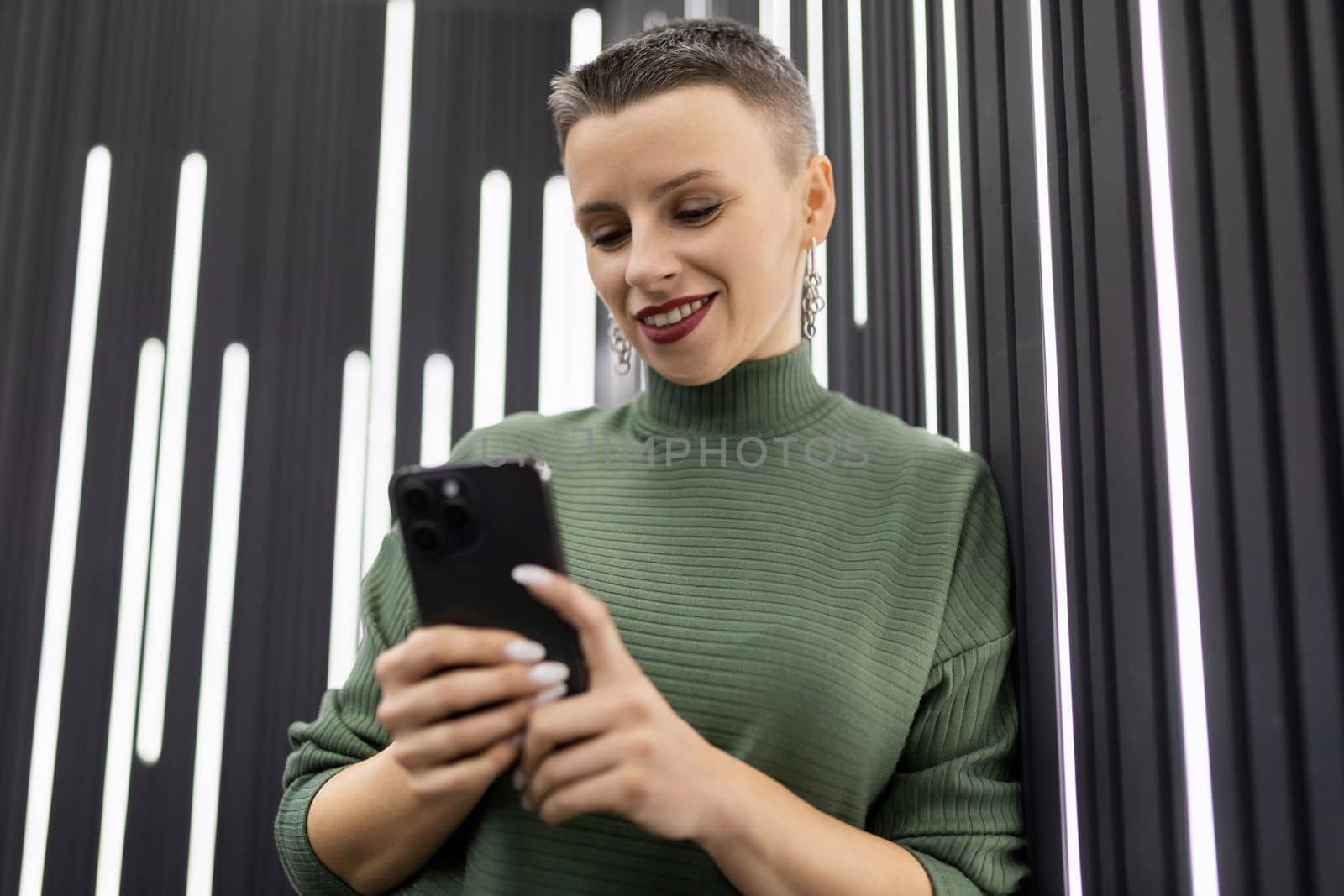 a woman with a short haircut with a phone in her hands against the background of a black wall with backlight.