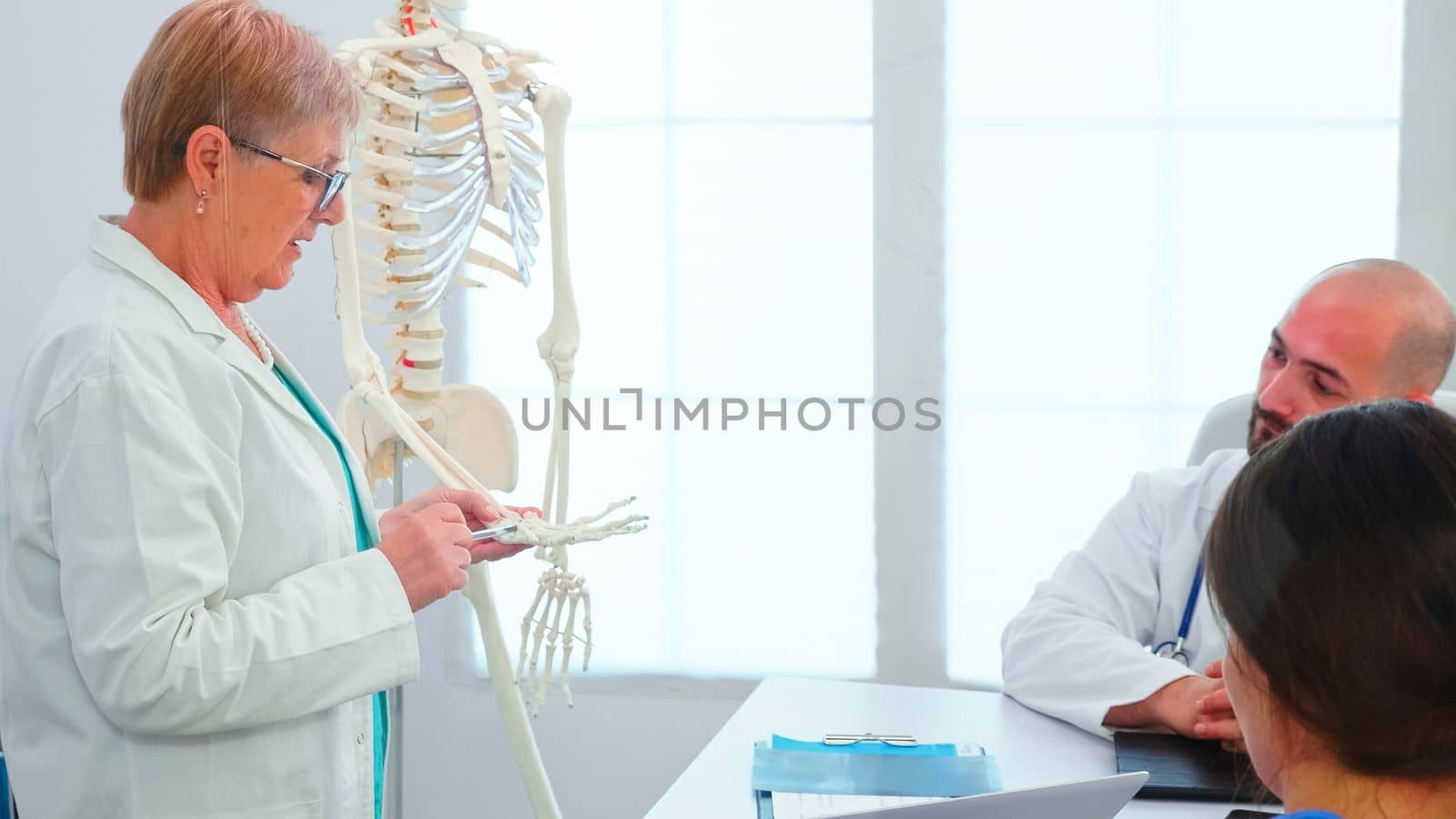 Female radiologist doctor holding presentation using skeleton in front of medical staff. Clinic expert therapist talking with colleagues about disease, medicine professional working in boardroom