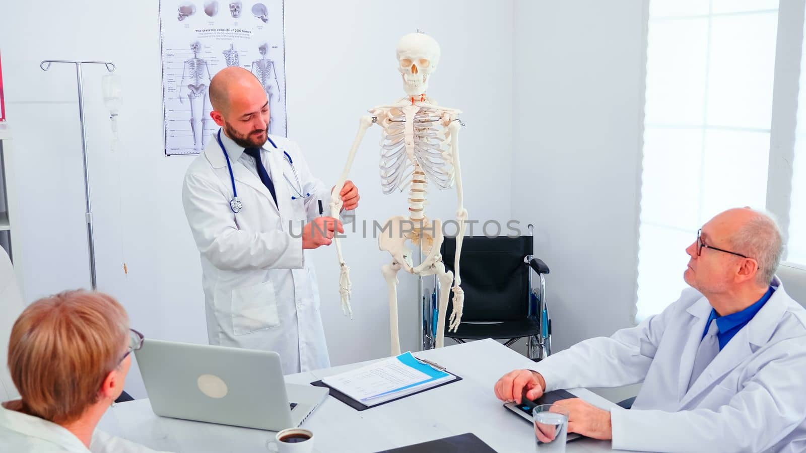 Expert doctor in radiology pointing at human skeleton during presentation in hospital conference room. Clinic therapist talking with colleagues about disease, medicine professional.