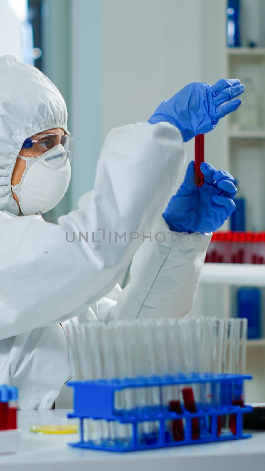 Researcher in coverall holding test tubes with blood sample for new treatment in medical laboratory. Team of doctors examining virus evolution using high tech for vaccine development against covid19