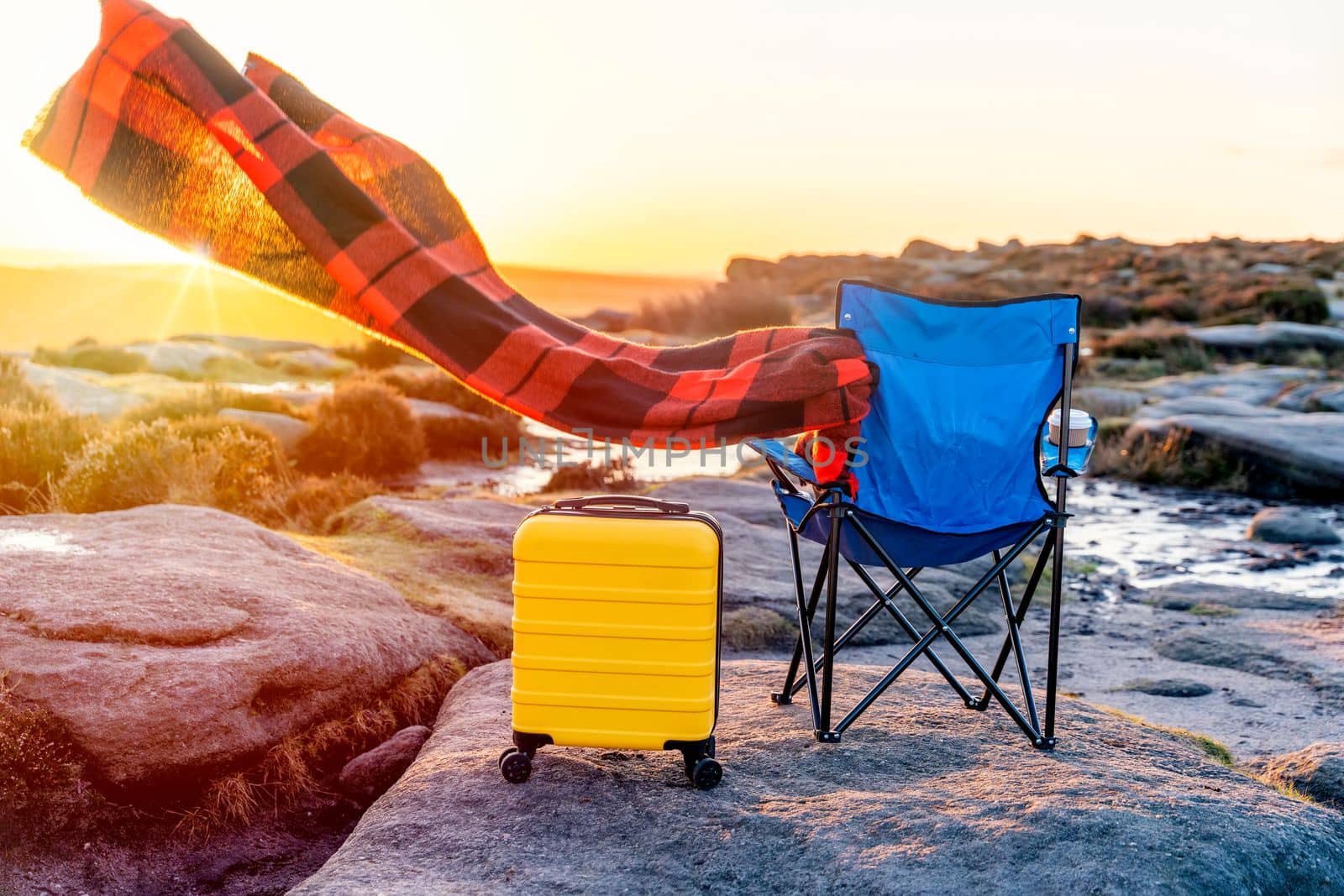 Blue beach chair, yellow Suitcase, orange scarf in the national park Peak District at sunrise. British cold winter. Local tourism concept.