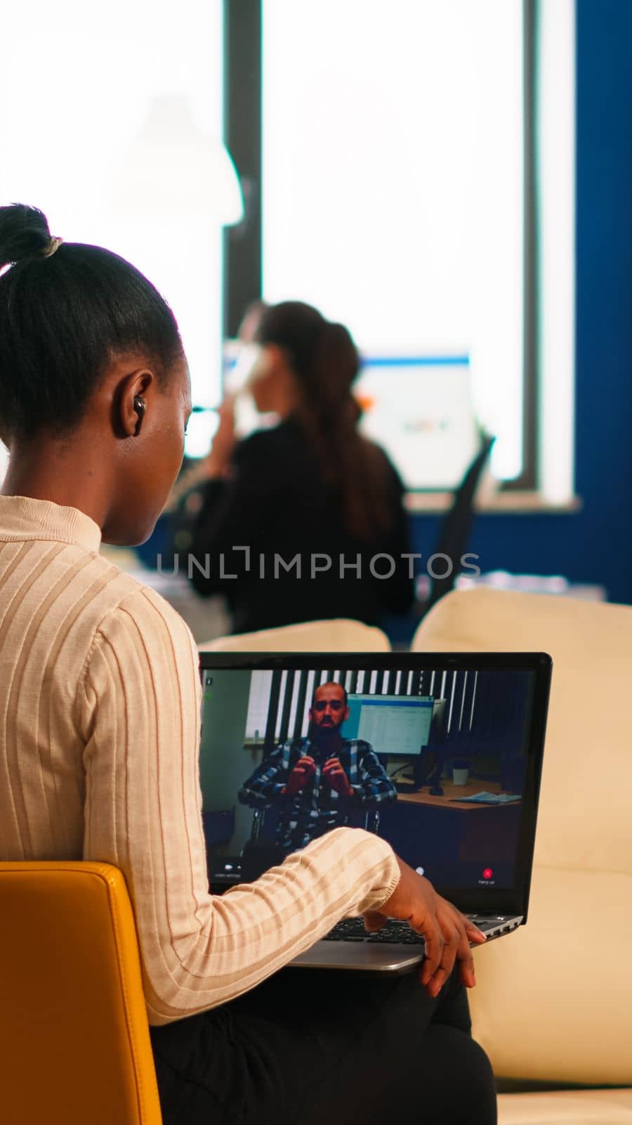 Black woman discussing with remote disabled colleague using video call holding laptop sitting on couch in business modern office. Diverse coworkers planning new financial project in modern company