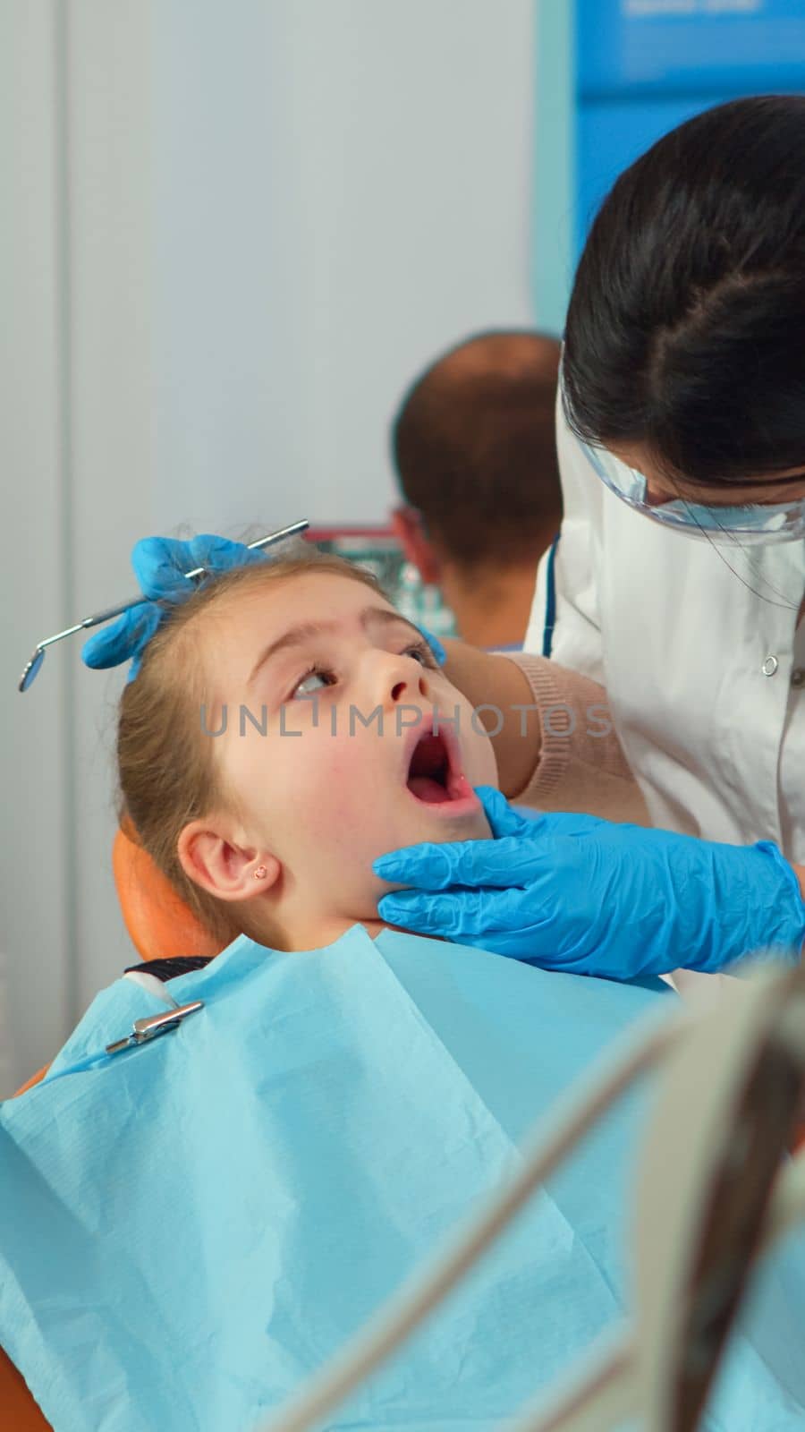 Pediatric dentist with mask treating teeth to little girl patient by DCStudio