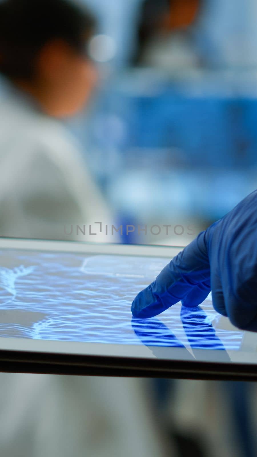 Close up of researcher using tablet, pointing, analysing DNA informations standing in medical laboratory. Viorolog doctor working to discover medical treatment, vaccine development, virus evolution