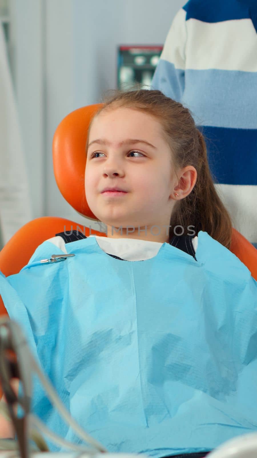 Close up of kid patient with toothache wearing dental bib talking with dentist by DCStudio