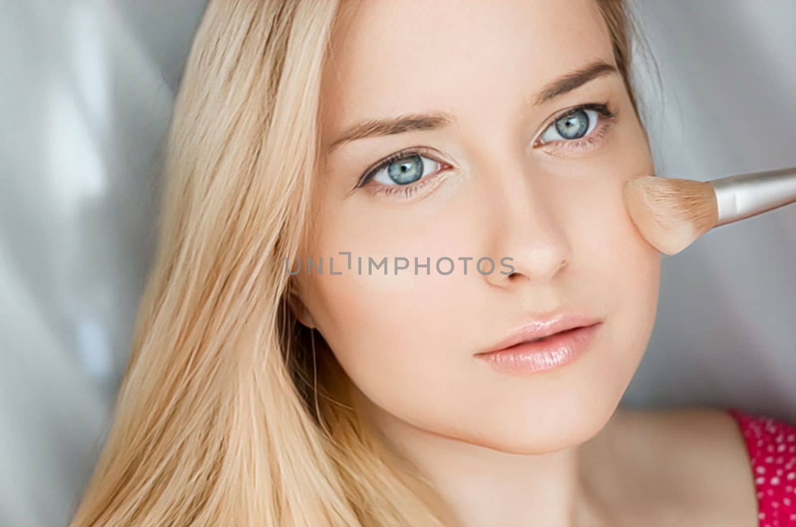 Beautiful blonde woman applying liquid make-up foundation on her skin with make-up brush.