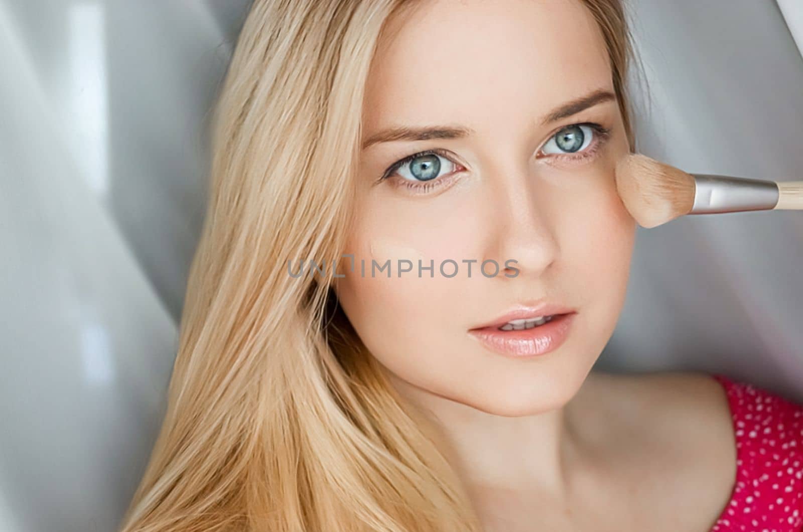 Beautiful blonde woman applying liquid make-up foundation on her skin with make-up brush.