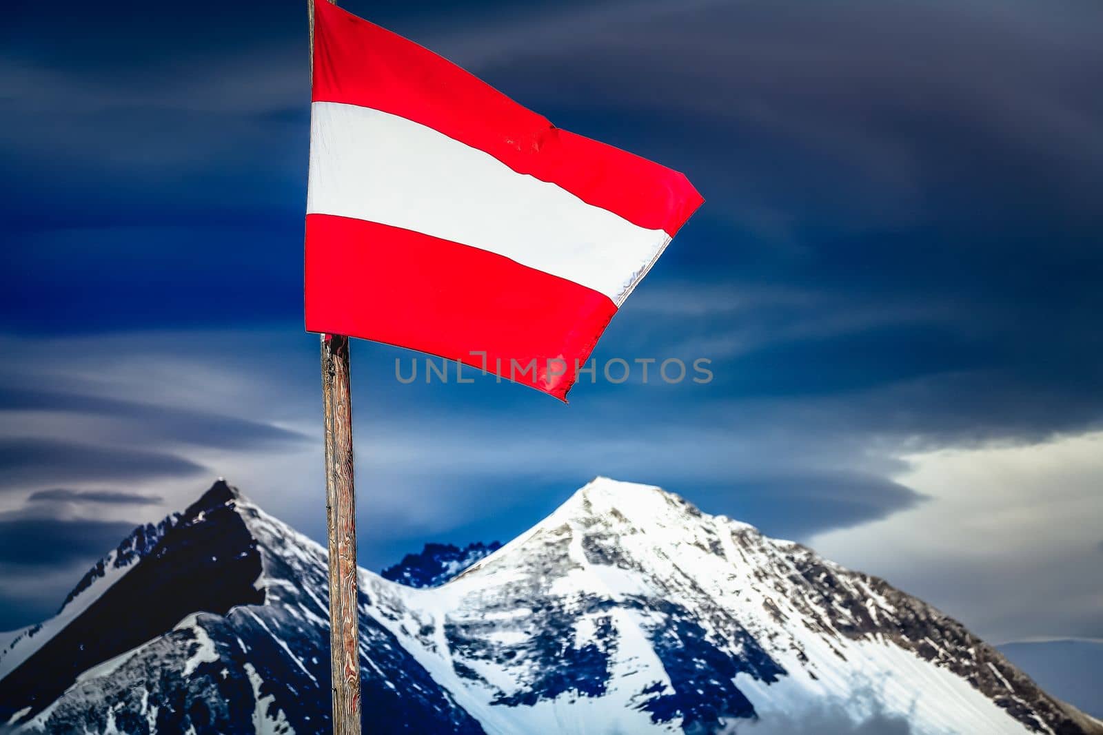 Austrian flag in Grossglockner National Park, snowcapped alps at dramatic sky, Austria