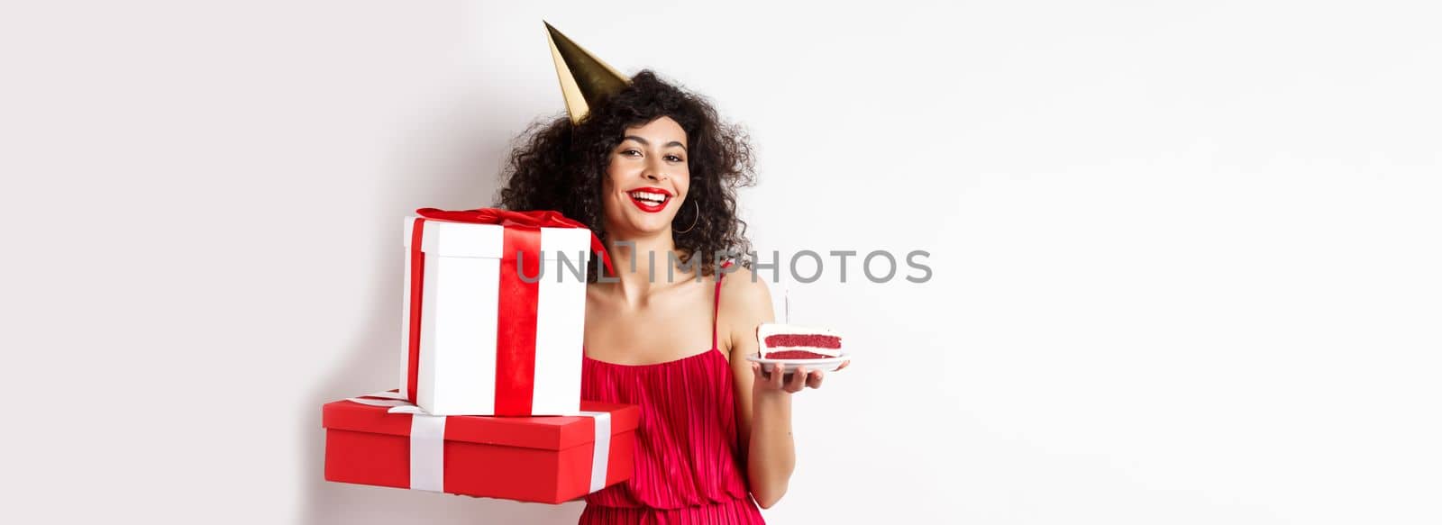 Happy birthday girl in red dress, celebrating and holding gifts with bday cake, standing on white background by Benzoix