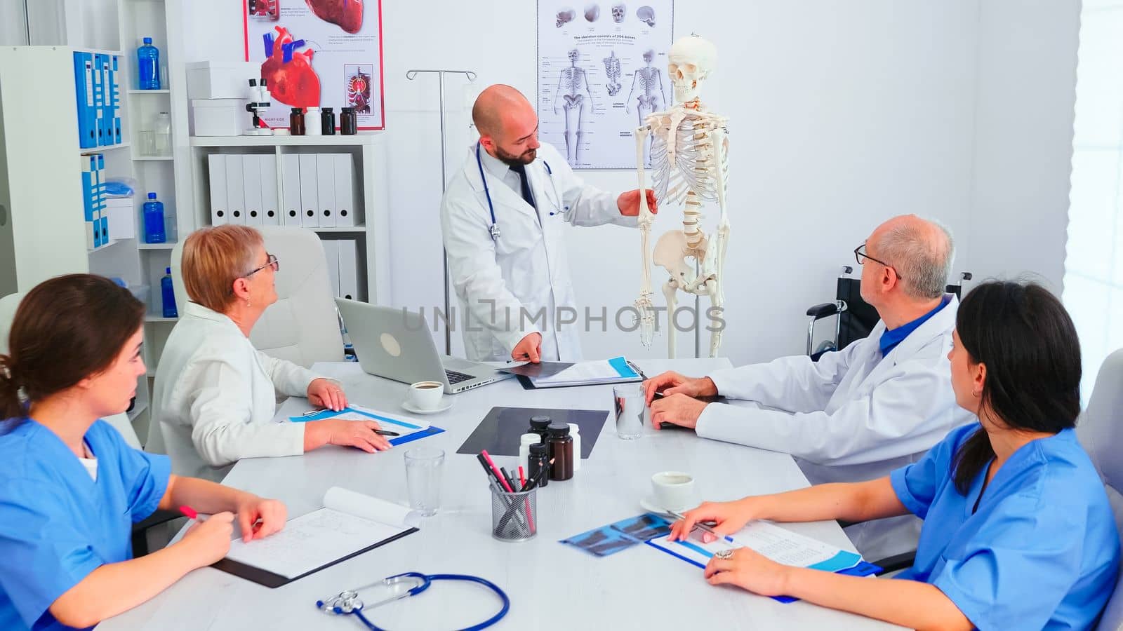 Doctor explaining radiography in front of medical staff in hospital conference room using human skeleton model. Clinic expert therapist talking with colleagues about disease, medicine professional