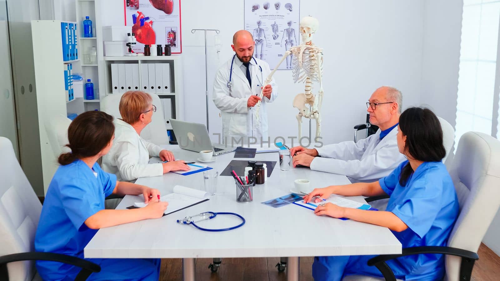 Expert doctor holding radiography during medical seminar for medical staff in conference room using human skeleton model. Clinic therapist talking with colleagues about disease, medicine professional