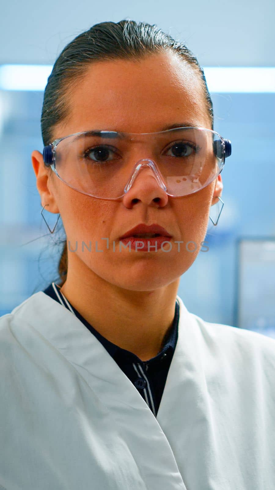 Tired chemist doctor looking at camera sighing in modern equipped lab. Multiethnic team examining virus evolution using high tech and chemistry tools for scientific research, vaccine development.