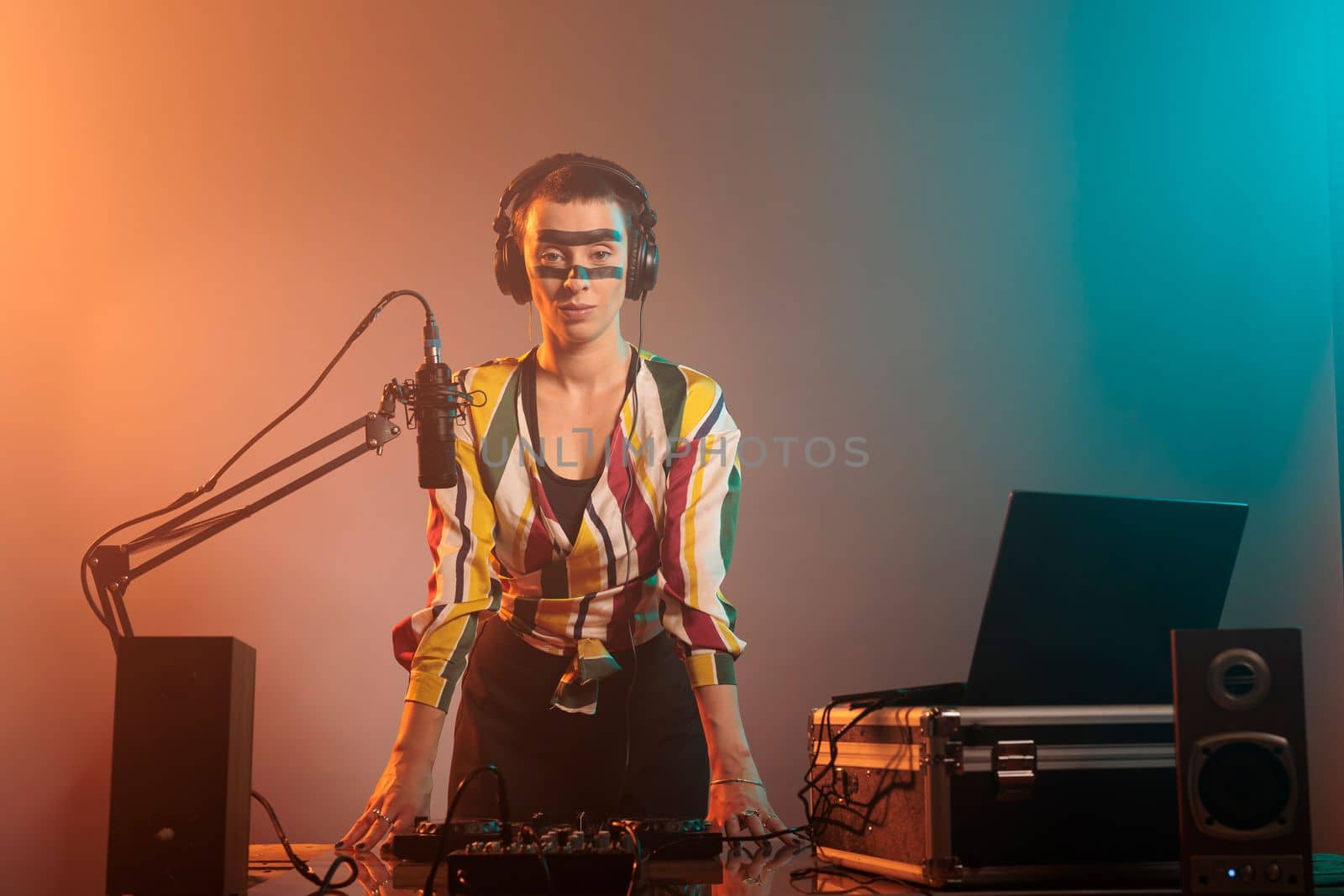 Musical artist with crazy make up having party to mix records and techno songs at tunrtables in studio. Using mixer to perform with audio equipment and stereo instrument, electronics.